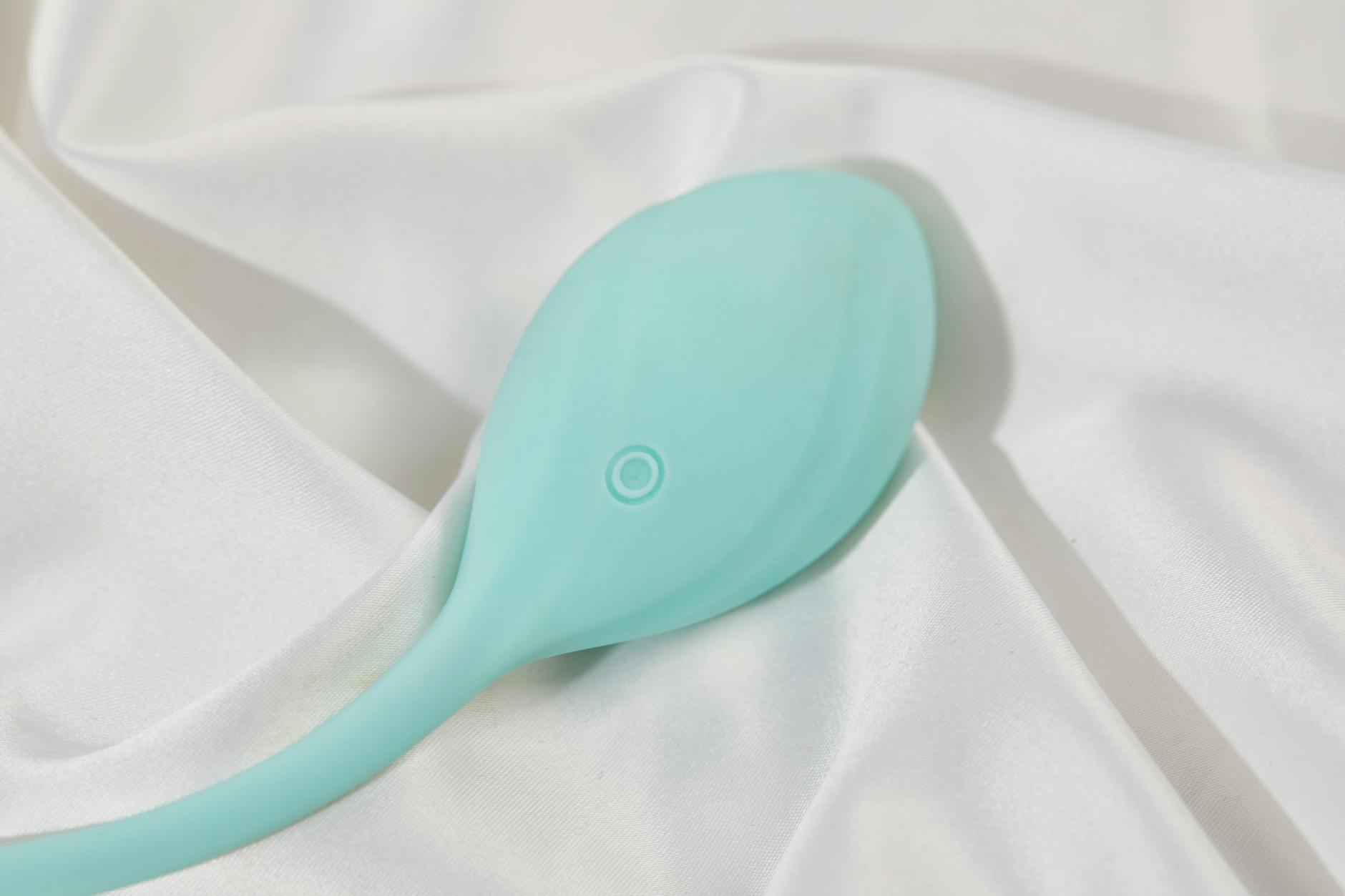 Stylish teal vibrator on white silk fabric