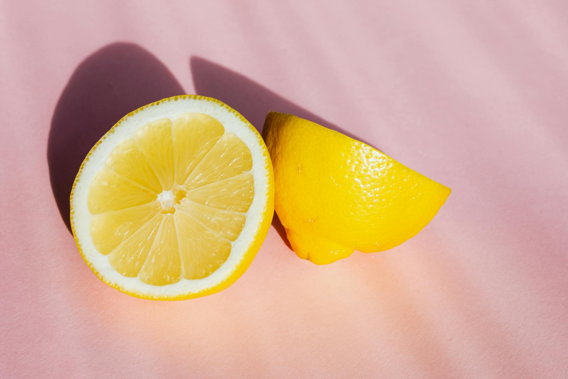 Fresh halved lemons in bright sunlight on pink background, symbolizing renewal and pleasure during hormonal shifts
