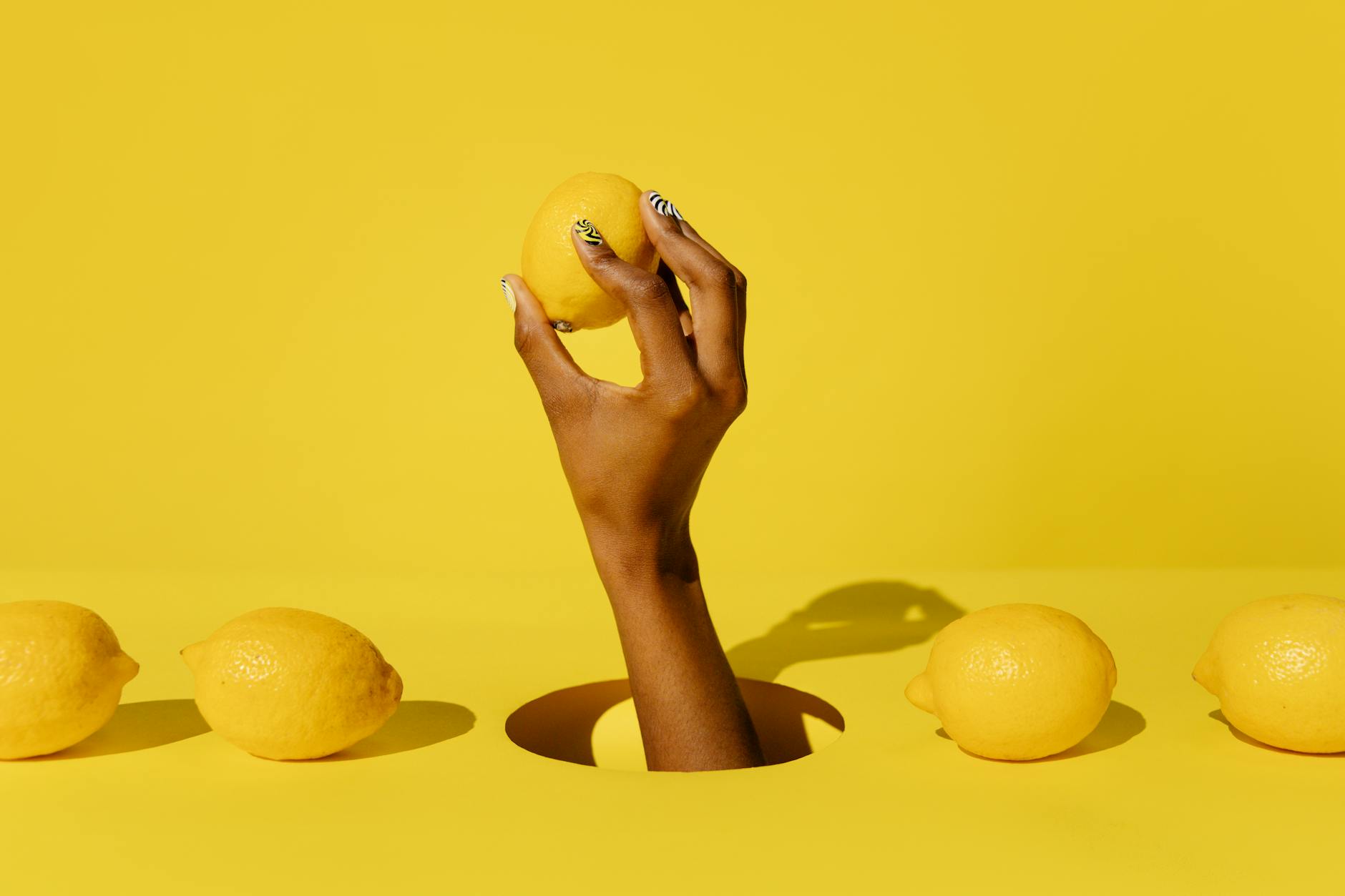 A hand holding a fresh lemon against a vibrant yellow background, symbolizing the natural approach to midlife pleasure.