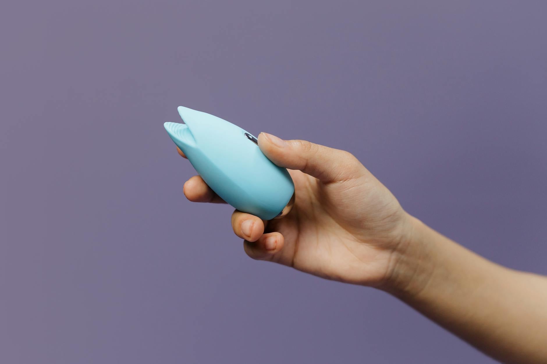 A close-up of hands holding a personal massager against a knitted sweater, symbolizing intimate connection between partners.