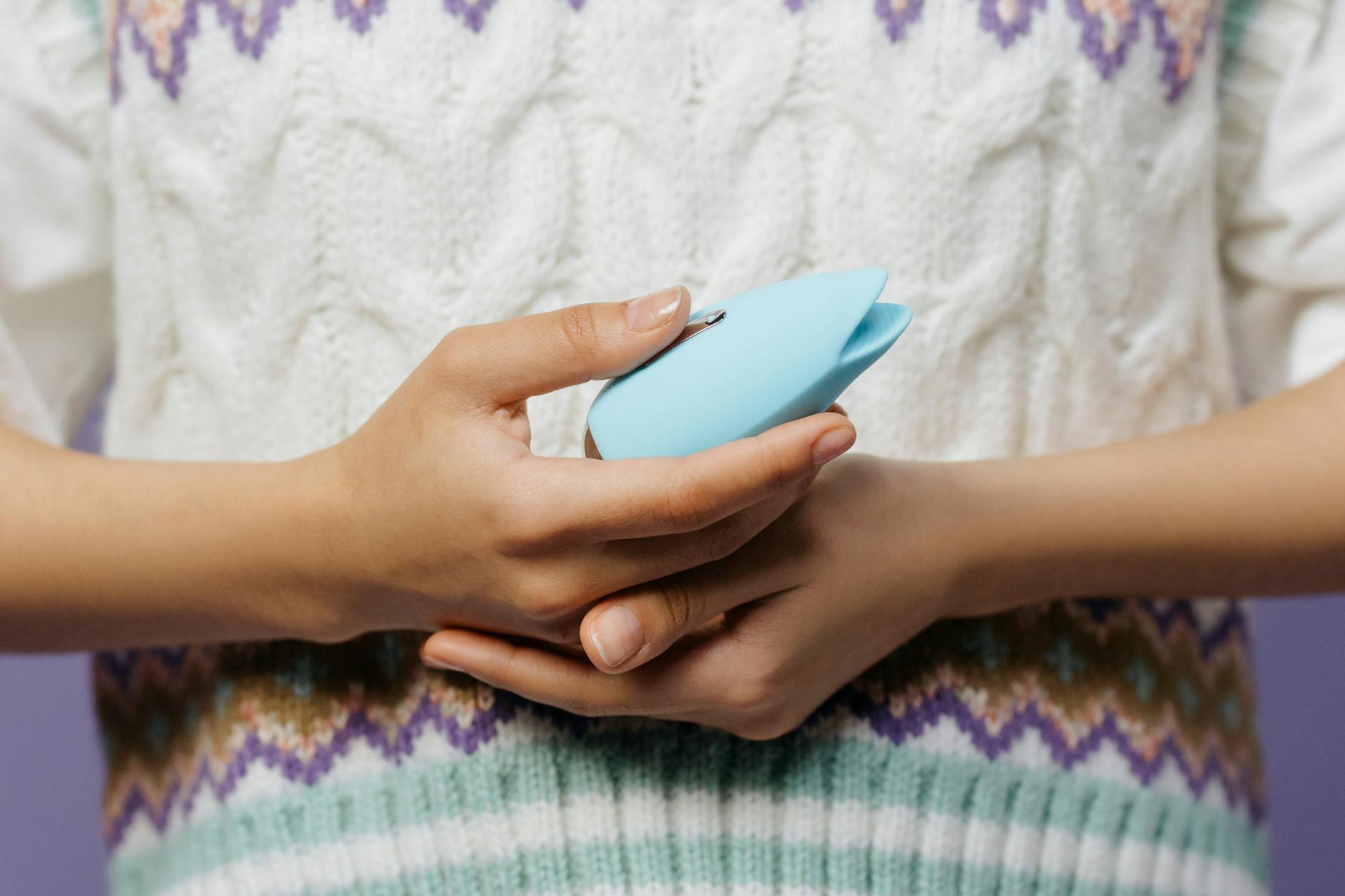 Gros plan des mains tenant un vibromasseur contre un pull tricoté