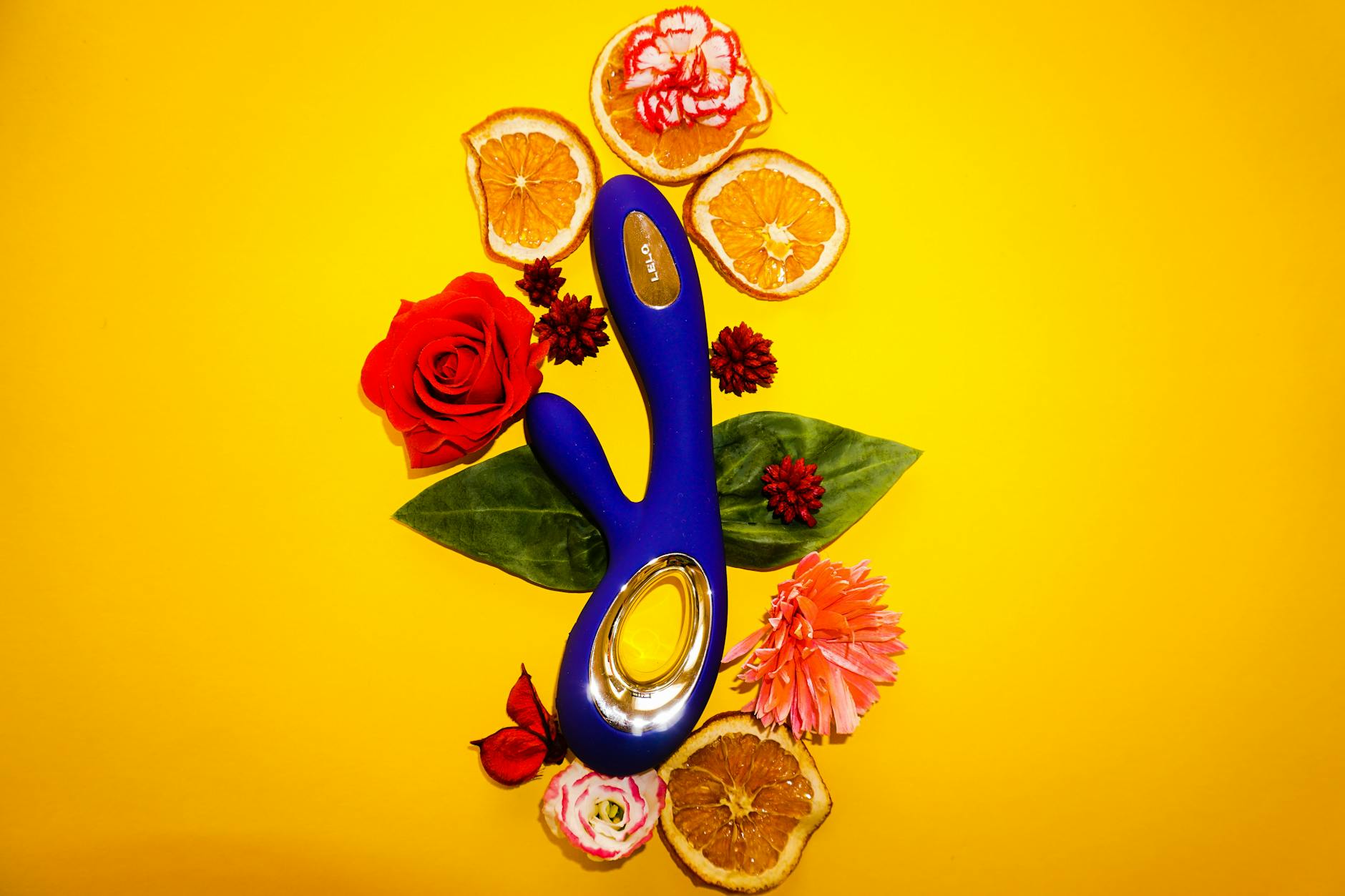 A blue clitoral vibrator surrounded by fresh lemons and citrus elements on a bright yellow background
